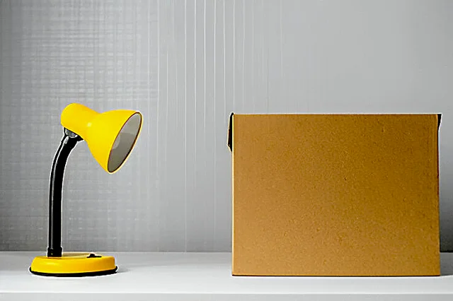 A yellow table lamp on a white floor with a brown box