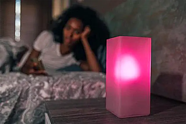 woman reading book on bed in light of a pink smart lamp